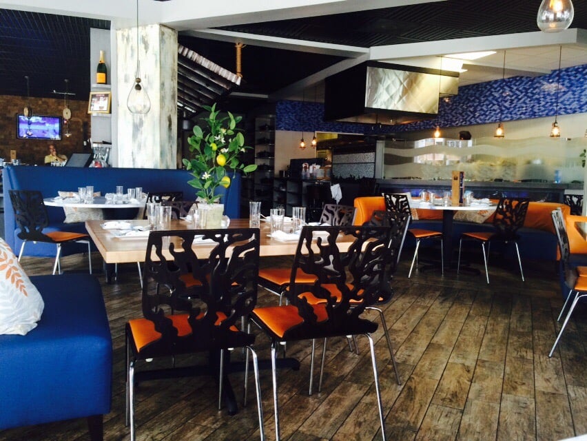 Dining room with blue banquettes, orange chairs, wood floors, and a lemon tree