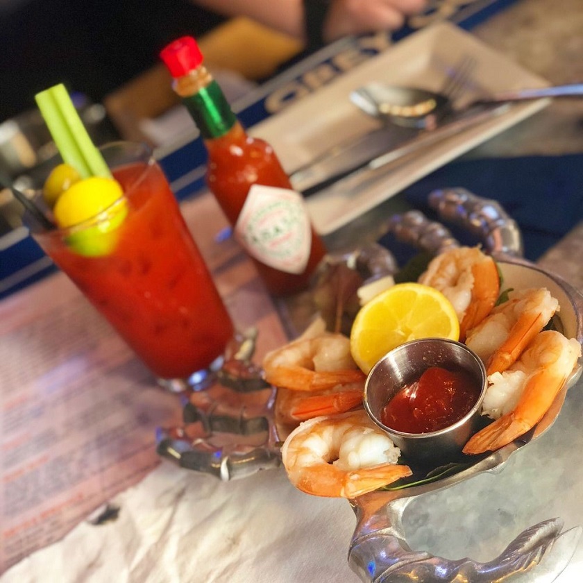 Jumbo shrimp cocktail with lemon and cocktail sauce, alongside a Bloody Mary