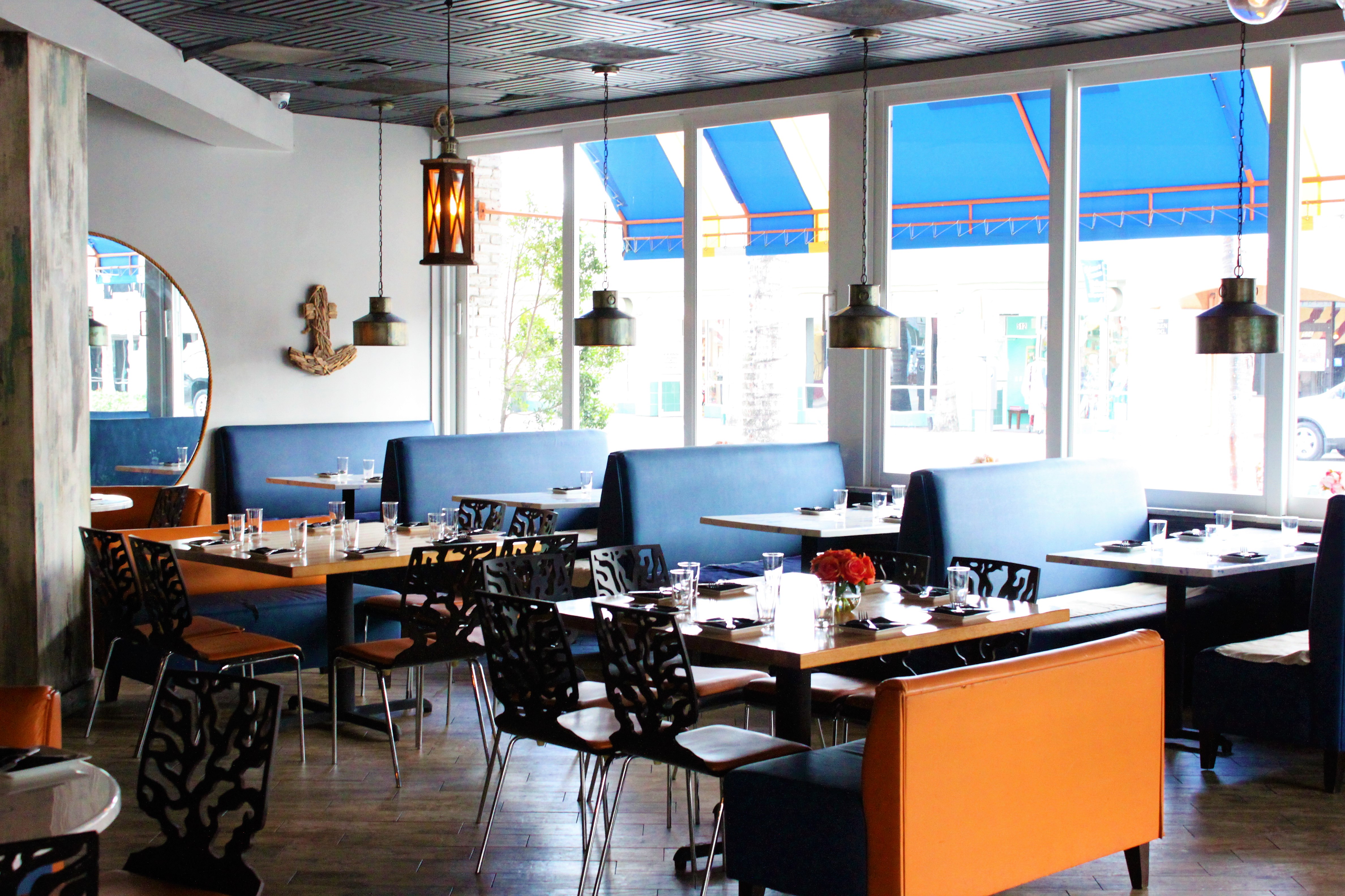 Dining area with blue banquettes, orange chairs, and Atlantic Avenue through the windows
