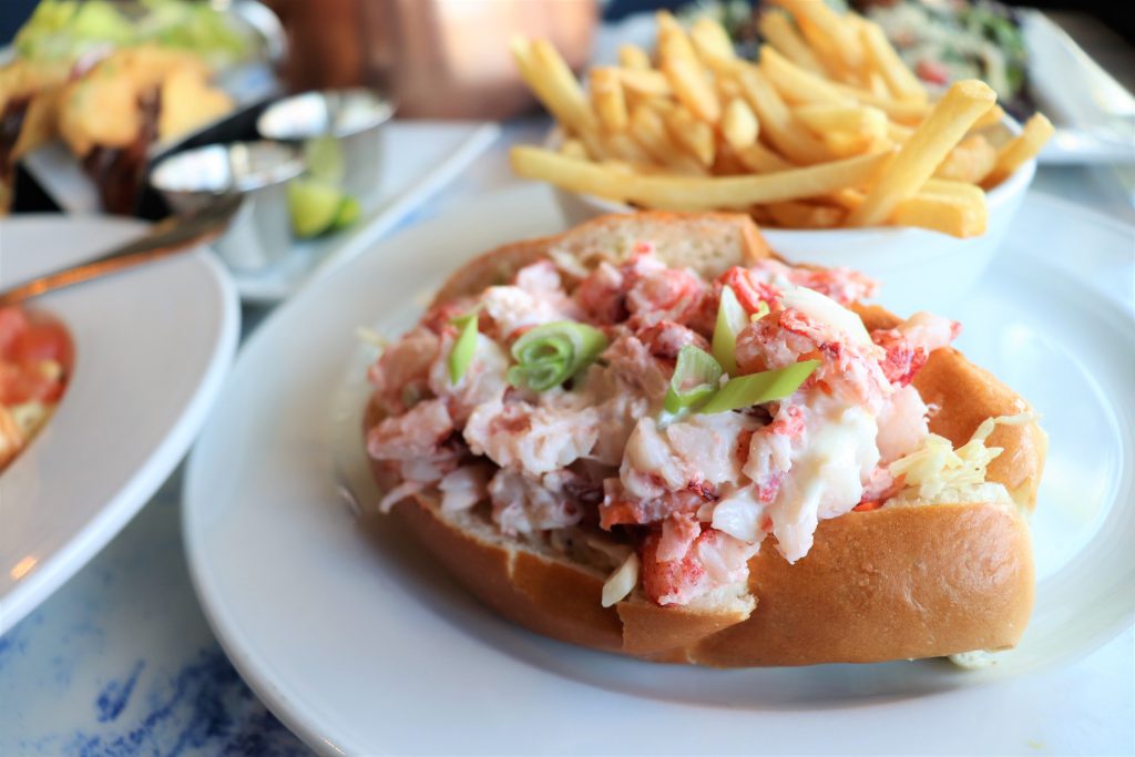 New England lobster roll on a toasted bun, piled with chunks of lobster meat and scallions, served with French fries